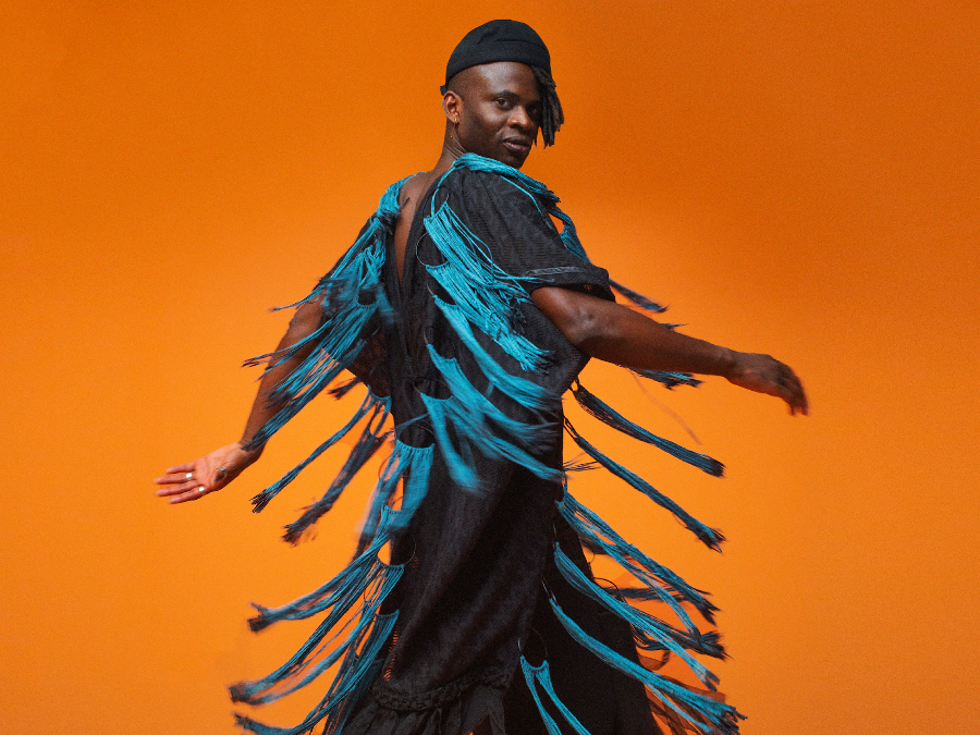 Wayne Snow mid-spin in a black tunic with long turquoise tassels during the COLORS session