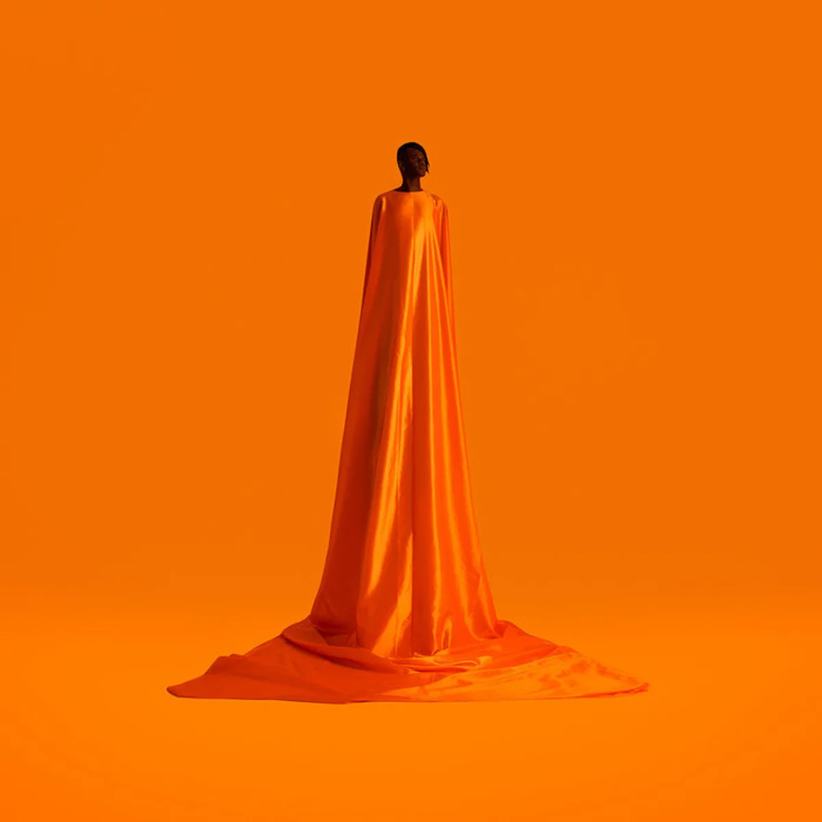 Figurine artwork — figure standing in a floor-length orange gown against a seamless orange backdrop
